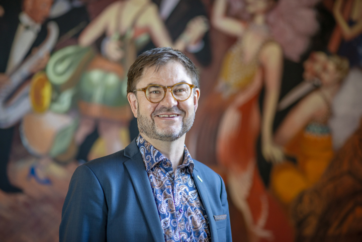 Mikael Flodström leende framför en färggrann bakgrund.