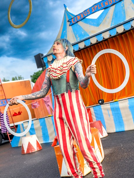 Cirkusartist i färgglada kläder jonglerar med ringar