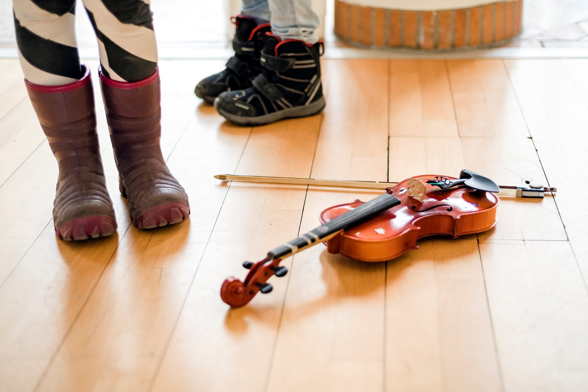 Två par barnskor och en fiol på ett golv