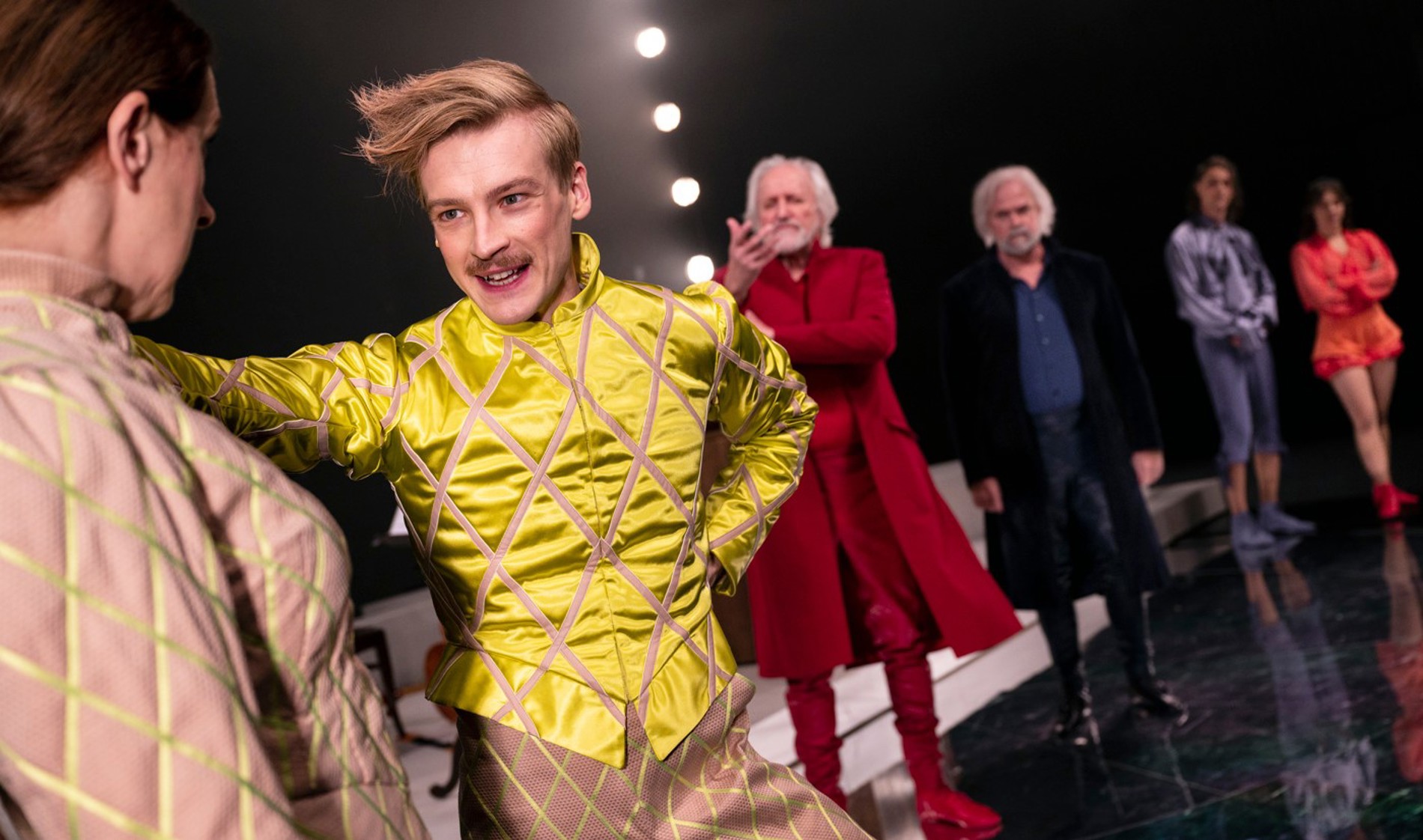 En teaterscen med sex skådespelare i färgglada kläder.