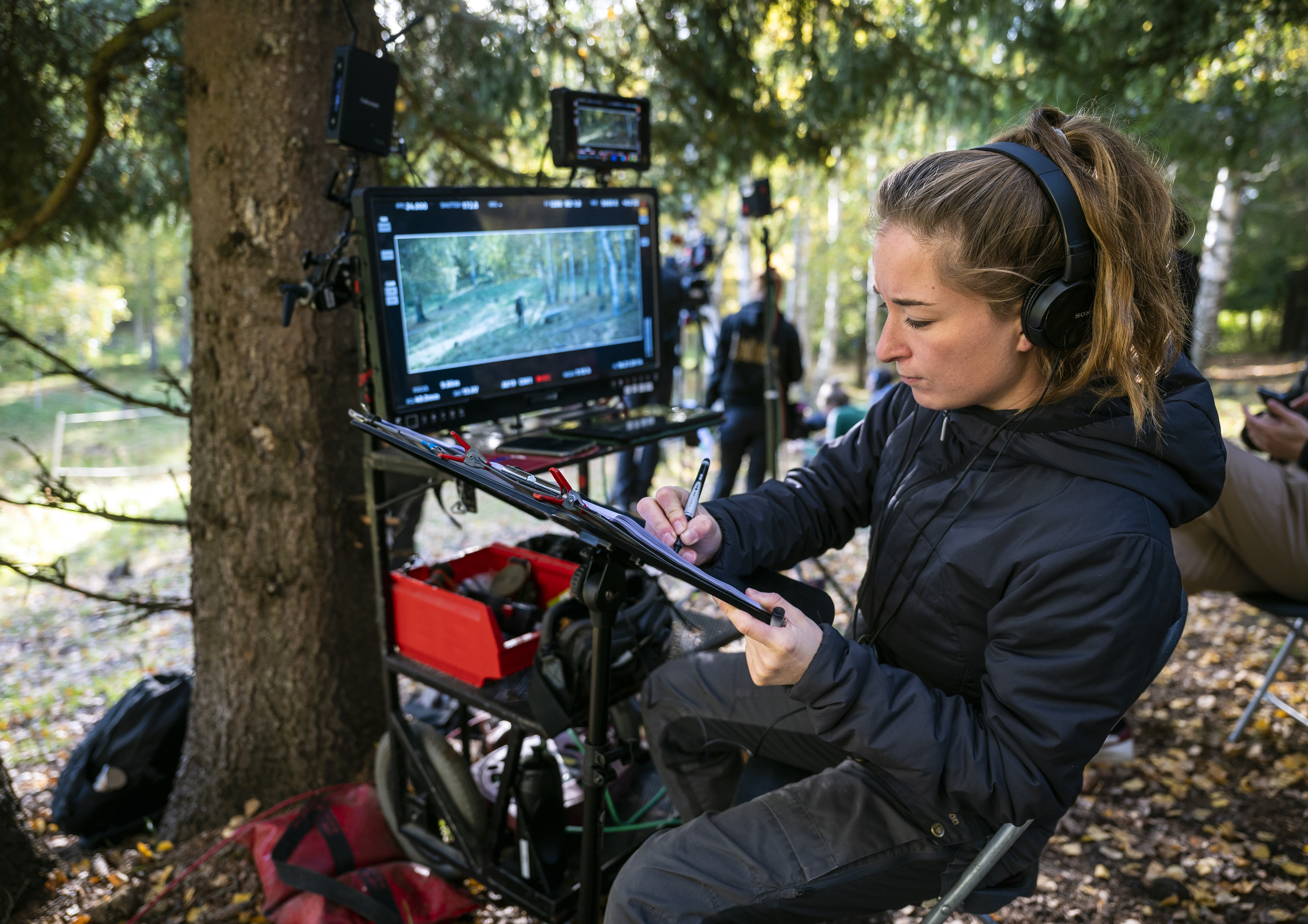 Kvinna med hörlurar som tittar på en skär i en skog, filminspelning pågår.