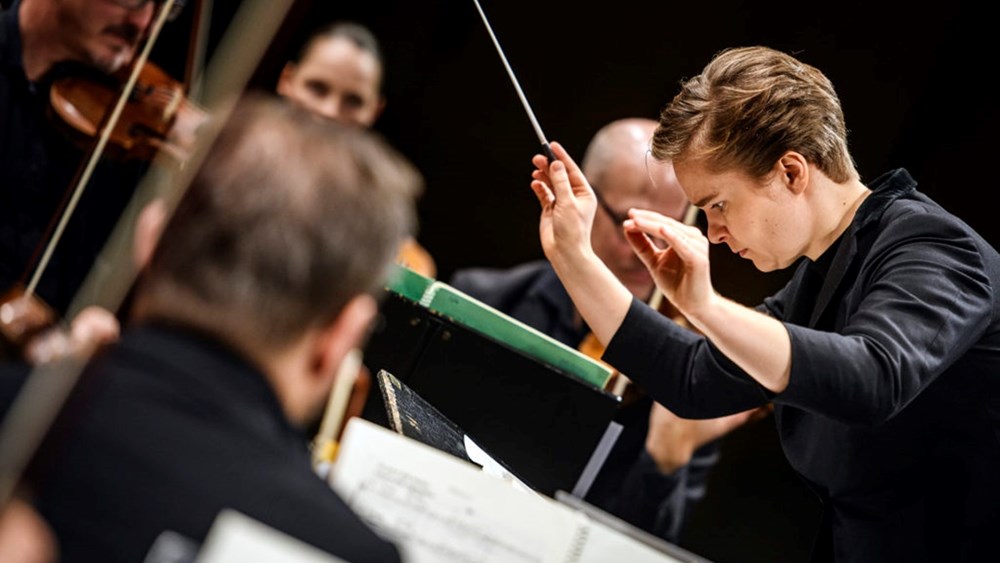 En svartklädd dirigent dirigerar Nordiska Kammarorkestern.