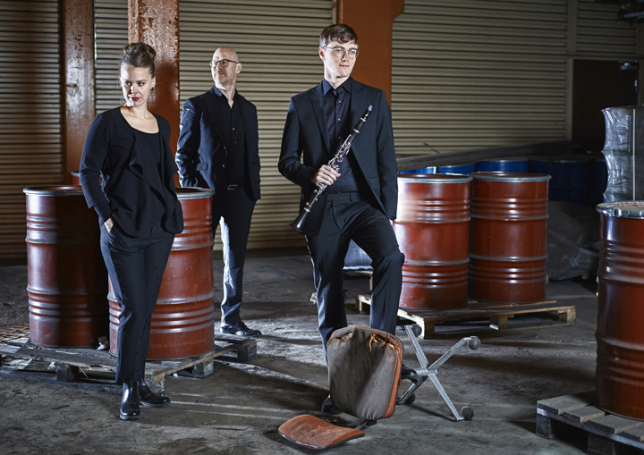 Tre svartklädda människor i en karg lokal