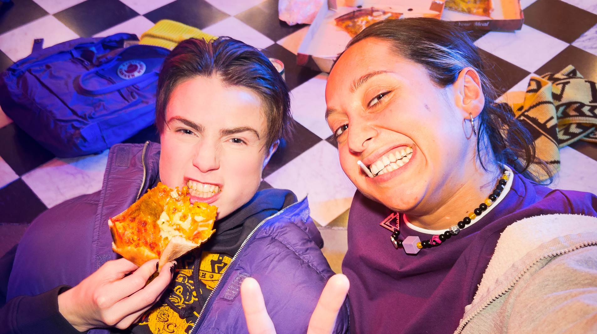 Två människor ligger på golvet och äter pizza samtidigt som de tar en selfie.